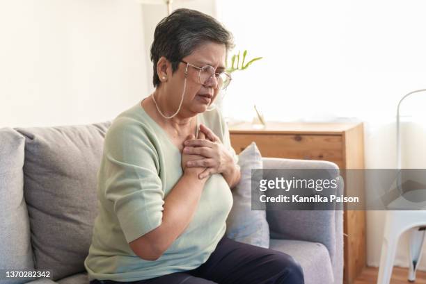 senior asian woman holding her chest in discomfort due to pain from heart attack. - chest pain stock pictures, royalty-free photos & images