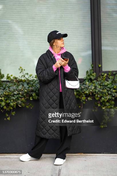 Guest wears a black with white embroidered inscriptions cap from Ksubi, a pink hoodie sweater from Jacquemus, a black quilted long puffer jacket, a...