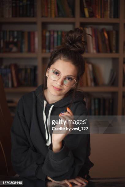 portrait of a teenage girl (14-15 years) wearing glasses in front of a bookcase - 14 15 years girl stock pictures, royalty-free photos & images