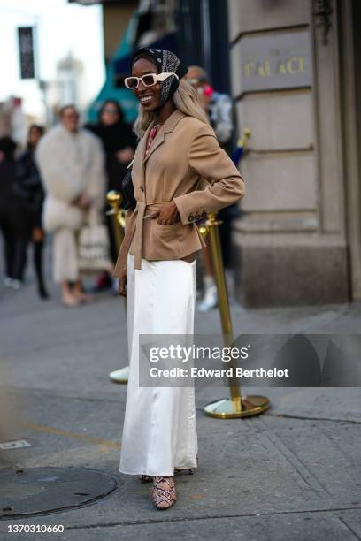 Guest wears a black and white print pattern silk scarf on the head, white sunglasses, a gold with large red and orange stones pendant necklace, a...