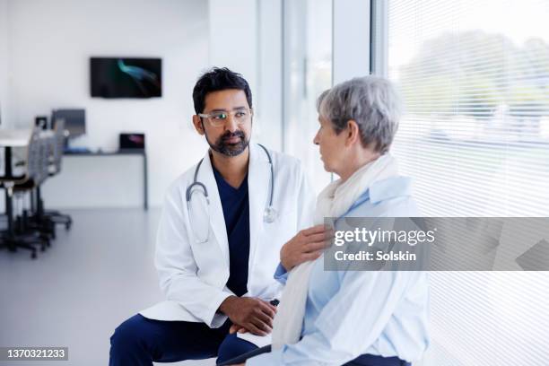 doctor and patient in conversation in hospital hallway - seguro médico fotografías e imágenes de stock