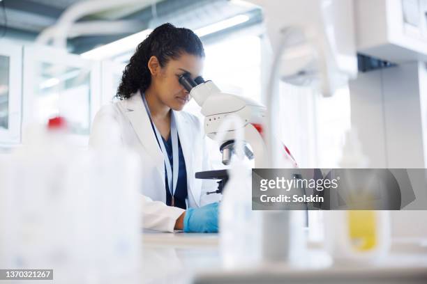 female scientist in laboratory looking into microscope - 微生物學 個照片及圖片檔