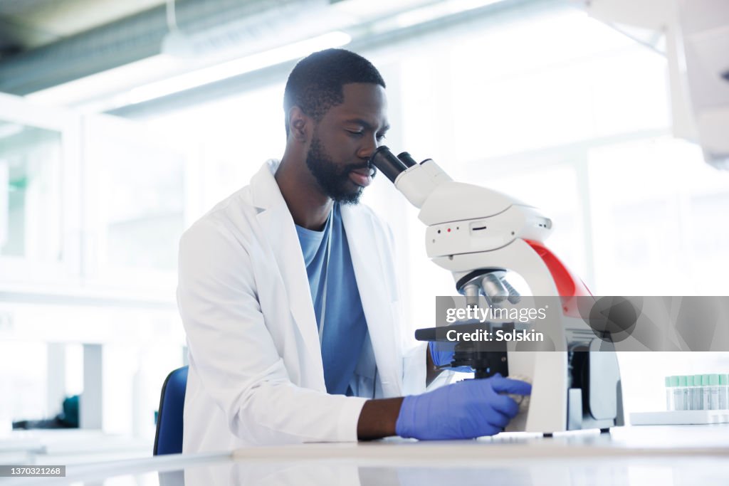 Male scientist working in laboratory, looking into microscope