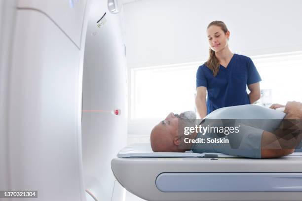 medical professional helping mature man in ct scanner - instrumento para diagnóstico imagens e fotografias de stock