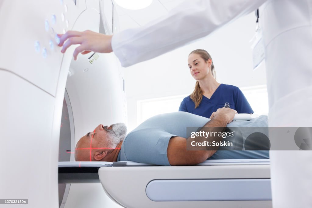 Medical professionals helping mature man in CT scanner