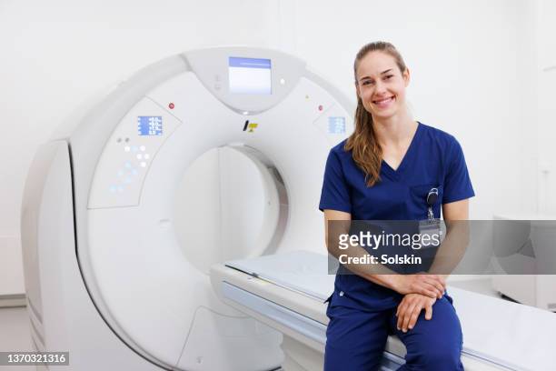 radiographer sitting on ct scanner bed - radioloog stockfoto's en -beelden