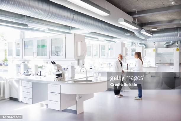 two scientists in conversation, standing in laboratory - laboratorio chimico foto e immagini stock