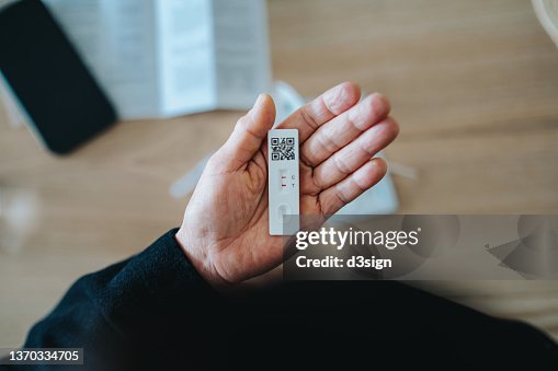 Overhead view of senior Asian woman carrying out a Covid-19 rapid lateral flow test at home. She is holding a positive Coronavirus rapid self test device, feeling worried Overhead view of senior Asian woman carrying out a Covid-19 rapid lateral flow test at home. She is holding a positive Coronavirus rapid self test device, feeling worried