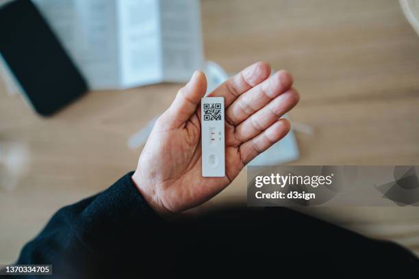 overhead view of senior asian woman carrying out a covid-19 rapid lateral flow test at home. she is holding a positive coronavirus rapid self test device, feeling worried - test photos et images de collection