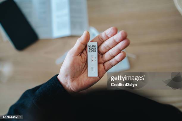 overhead view of senior asian woman carrying out a covid-19 rapid lateral flow test at home. she is holding a positive coronavirus rapid self test device, feeling worried - coronavirus stock pictures, royalty-free photos & images