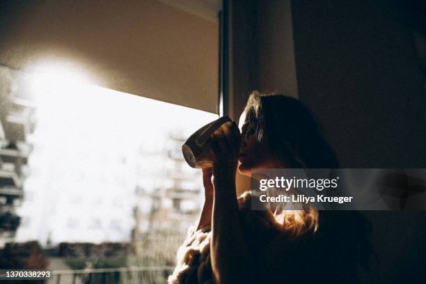 middle-aged woman enjoying her morning coffee. - happy woman in early morning sunlight photos et images de collection