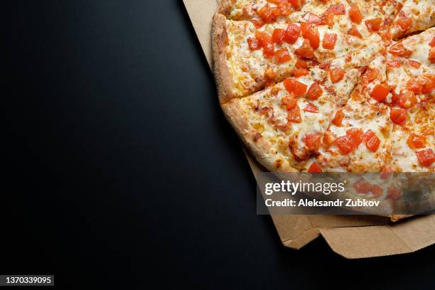 italian pizza in a pizza box and for delivery, on a black background or table. pizza margarita with tomatoes and cheese, cut into pieces, without meat. the concept of vegetarian food, fast unhealthy food. delivery to your home or work. copy space. - geheel stockfoto's en -beelden