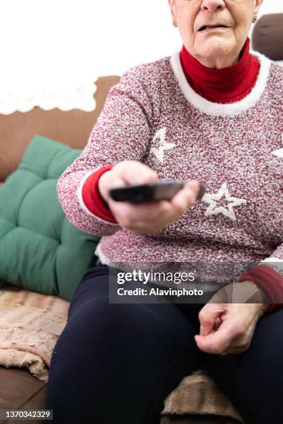 elderly woman in the living room at home with the remote control of the television - aburrimiento stock-fotos und bilder