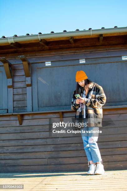 teenage woman with orange wool hat using her smartphone in the street - checked shirt fotografías e imágenes de stock