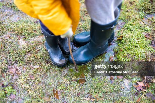 young woman & young girl wearing matching tall navy rubber boots play in a muddy puddle at home - puddle stock pictures, royalty-free photos & images