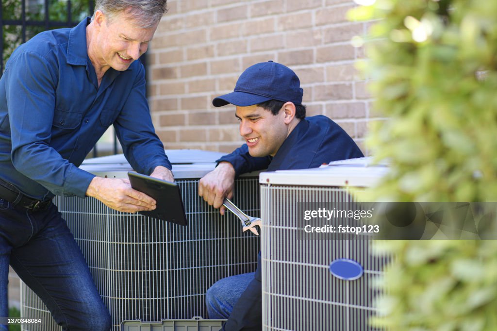 Multi-ethnic team of blue collar air conditioner repairmen at work.