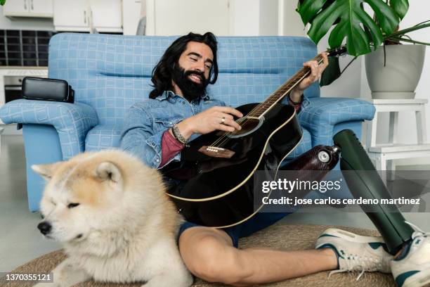 disabled man practices playing guitar at home on the couch with his dog - amputee home stock pictures, royalty-free photos & images