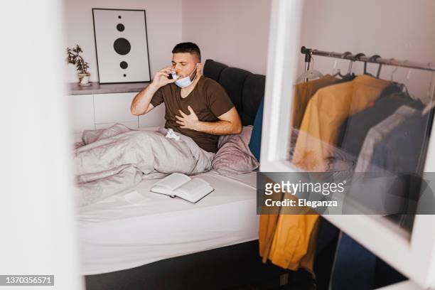 young man using asthma inhaler at home - copd stockfoto's en -beelden
