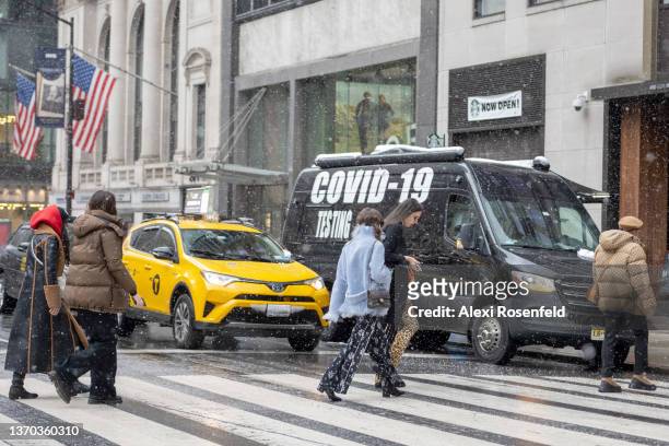 People leaving the Ulla Johnson Show walk across the road in front of a Yellow cab and COVID-19 testing site on February 13, 2022 in New York City