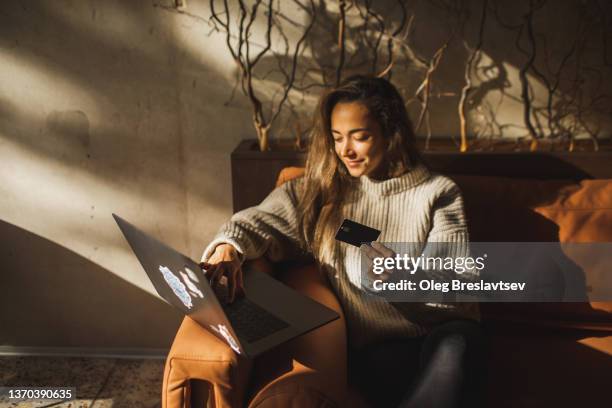 young smiling woman making online purchases in cafe with credit card and laptop - compras em casa imagens e fotografias de stock