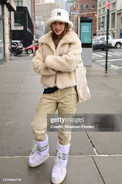 Guest wears a short teddy jacket, white moon boots and a blush white teddy bucket hat at Spring Studios at New York Fashion Week: The Shows on...