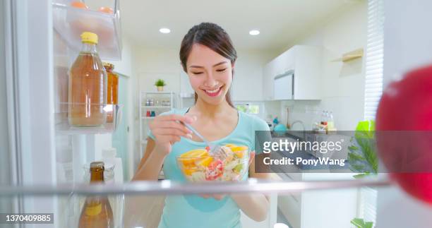 woman takes salad from refrigerator - fridge full of food stockfoto's en -beelden