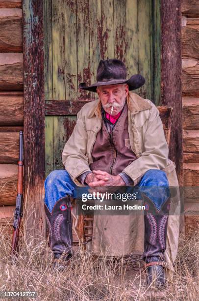 a cowboy poses outside of a rustic cabin - cowboy spurs stock pictures, royalty-free photos & images