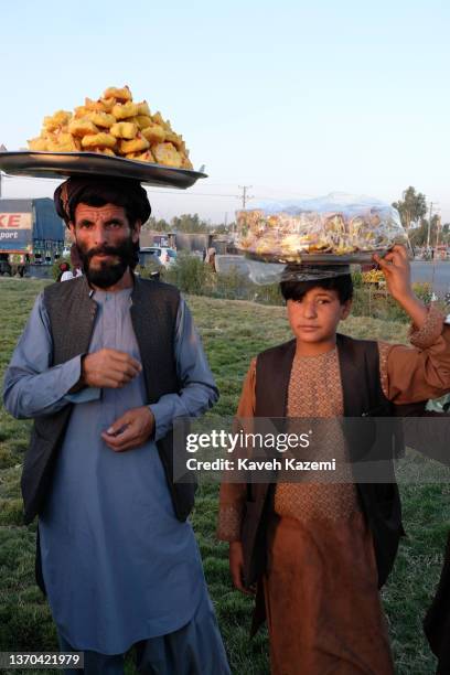 Young boy and a man carry pastries on trays placed over their heads in one of main squares in the city on September 22, 2021 in Kandahar, Afghanistan.