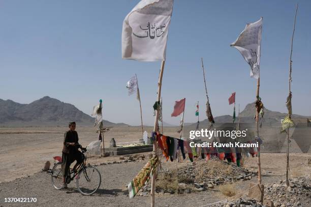 Young Pashtun boy rides on a bicycle by a roadside Taliban cemetery where Islamic Emirate of Afghanistan white flags are seen amass over the tombs of...