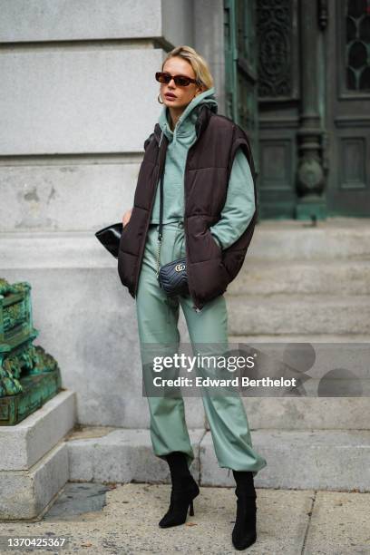 Model wears brown sunglasses, a green hoodie cropped sport pants, matching green high waist leather large pants, a dark brown chocolat sleeveless...