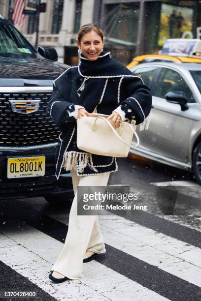 Jenny Walton wears an oversized blue scarf-style top with liner, white pants, and carries a cream purse at the Ulla Johnson show at New York Public...