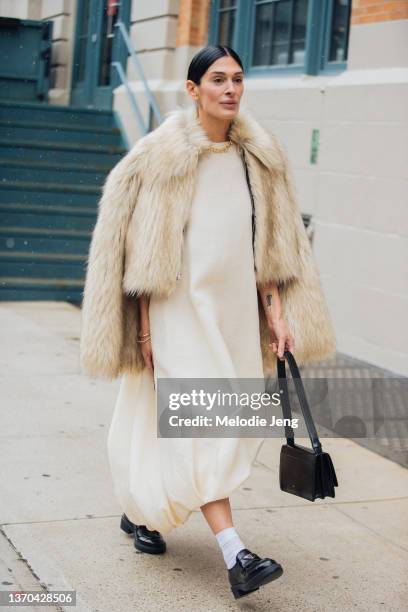 Athena Calderone wears a tan fur jacket, over a cream Khaite dress, white socks, black Prada oxford shoes, and a black purse at the Khaite show on...