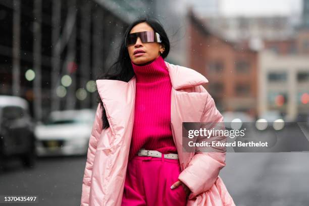 Miki Cheung wears black futurist sunglasses, a neon pink turtleneck pullover, a white leather belt from Saint Laurent Paris, matching neon pink large...
