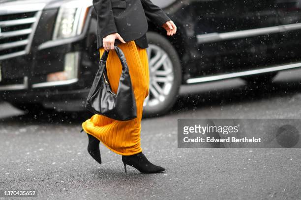 Olivia Perez wears a dark gray blazer jacket, a yellow ribbed long skirt, a black shiny leather zipper puffy handbag, black suede pointed heels ankle...
