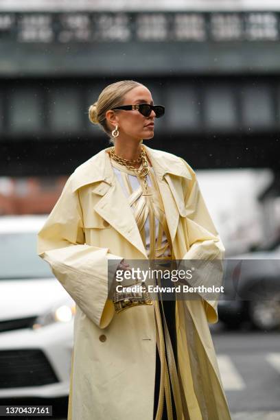Leonie Hanne wears black sunglasses from Balenciaga, a gold large double chain necklace, a pale yellow leather fringedlaces corset / top, a white...
