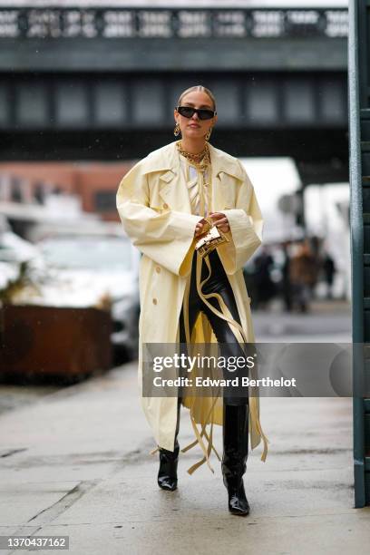 Leonie Hanne wears black sunglasses from Balenciaga, a gold large double chain necklace, a pale yellow leather fringedlaces corset / top, a white...