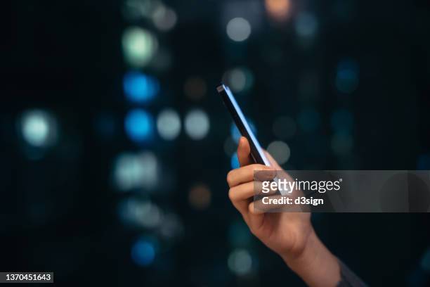 close up shot of female hand using smartphone at night, against illuminated and defocused bokeh in background. lifestyle and technology - movie still stock-fotos und bilder