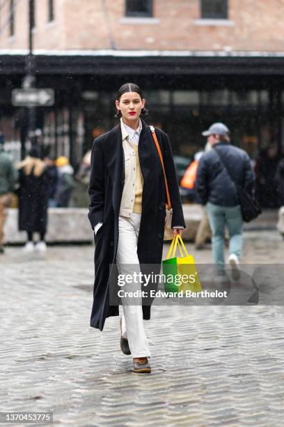 Model wears a white striped print pattern shirt, a pale yellow wool pullover, a beige shirt jacket, a black long coat, an orange shiny leather and...