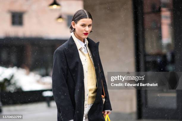 Model wears a white striped print pattern shirt, a pale yellow wool pullover, a beige shirt jacket, a black long coat, an orange shiny leather and...