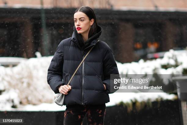 Model wears a black hoodie sweater, a black puffer jacket, a gray leather Chanel 2.55 crossbody bag, black and brown tie and dye print pattern flared...