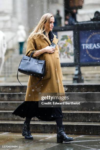 Guest wears a black scarf, a beige oversized coat, a black shiny leather Sac Du Jour handbag from Saint Laurent, a black long dress, black tights,...