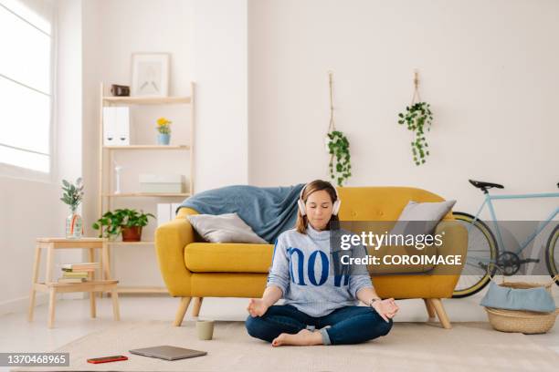 woman using headphones while meditating at home. - chica salon movil fotografías e imágenes de stock