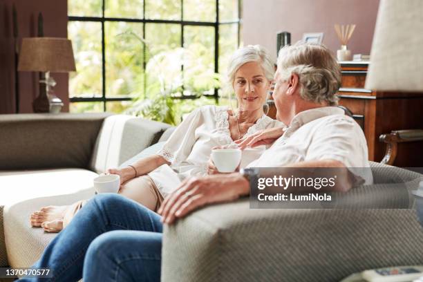 shot of a mature couple drinking coffee while relaxing together on a sofa at home - contemporary couple stock pictures, royalty-free photos & images