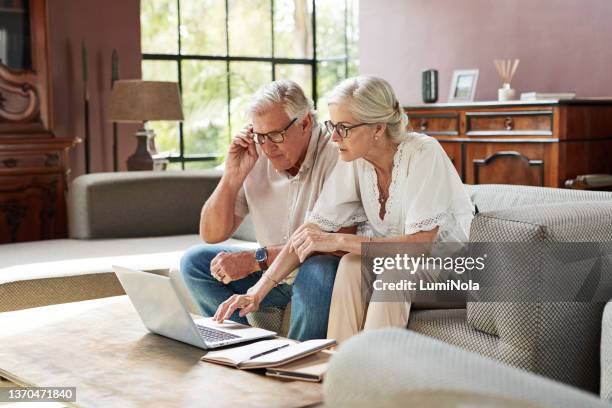 shot of a mature couple using a laptop while calculating their finances together at home - 2021 planning stock pictures, royalty-free photos & images