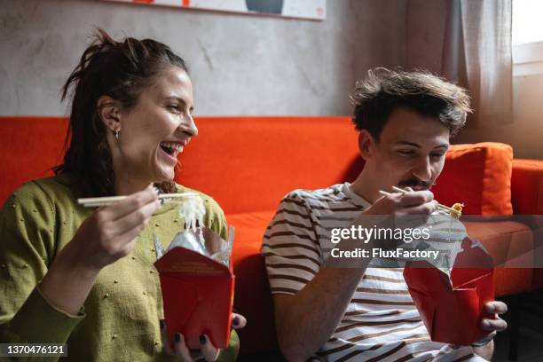 happy young couple enjoy the chinese take out food, while sitting on the floor - chinese takeout 個照片及圖片檔