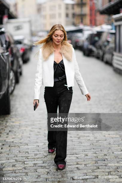 Guest wears a black V-neck satin t-shirt, a white leather with brown fur collar jacket, black denim jeans pants, burgundy shiny leather ankle boots,...