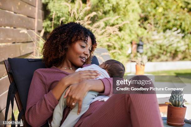 lächelnde mutter, die ihren kleinen jungen in ihren armen hält, während sie sich draußen entspannt - cute black newborn babies stock-fotos und bilder