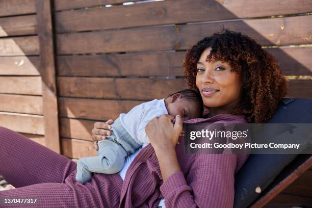 mama lächelt, während sie ihr schlafendes baby draußen auf einer terrasse hält - black mother holding newborn stock-fotos und bilder