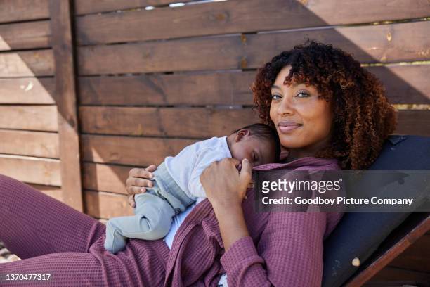 mom smiling while holding her sleeping baby outside on a patio - black mother and baby stock pictures, royalty-free photos & images