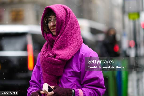 Guest wears a purple wool oversized fringed scarf, glasses, a purple nylon bomber coat, brown wool mittens, a pale pink and red print pattern cotton...